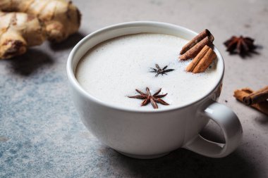 Beyaz fincanda tarçın, zencefil ve yıldız anasonlu ev yapımı Chai latte, yakın plan, koyu arka plan..