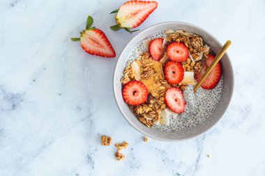 Ev yapımı hindistan cevizi taneli puding, fıstık ezmesi ve gri kasede çilek, mermer arka plan, üst manzara. Sağlıklı bitki temelli diyet, detoks, yaz tarifi.