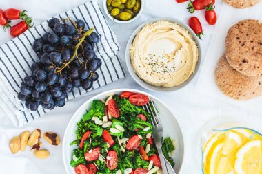 Vejetaryen piknik yemekleri: humus, limonata, brokoli salatası ve çimenlerin üzerinde beyaz bir battaniye üzerinde meyveler..