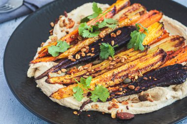 Siyah tabakta humus bulunan çok renkli fırında havuç. Vegan tarifi.