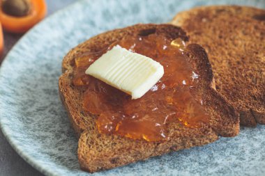 Gri bir tabakta tereyağlı ve kayısı reçelli tost..