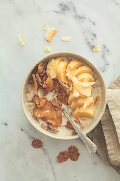 バナナ ココナッツチップ ピーナッツバターをボウルに入れた全粒穀物フレーク 白い背景 トップビュー 健康的な朝食のコンセプト ストック写真