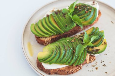 Beyaz bir tabakta krem peynirli ve avokadolu kahvaltı tostu. Sağlıklı gıda konsepti.