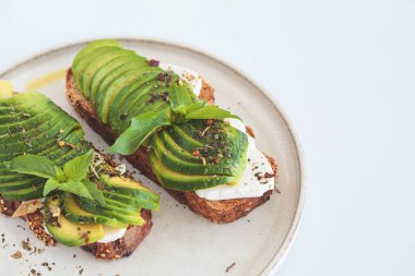 Beyaz bir tabakta krem peynirli ve avokadolu kahvaltı tostu. Sağlıklı gıda konsepti.