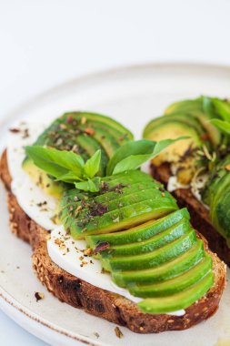 Krem peynirli tost ve beyaz tabakta avokado, beyaz arka plan, yakın plan. Sağlıklı gıda konsepti.