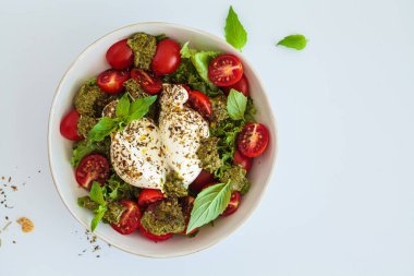 Burrata salad with cherry tomatoes, pesto and spices in a bowl on a white background, top view. clipart