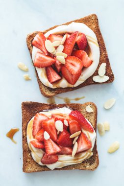 Flat lay of breakfast toasts with ricotta, strawberries and almonds on a white marble background.