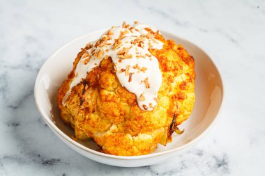 Tam kavrulmuş baharatlı karnabahar tahini soslu ve karamelli soğanlı, yakın plan..