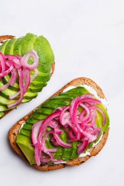 Krem peynirli avokado tostu ve beyaz tabakta turşulu soğan..
