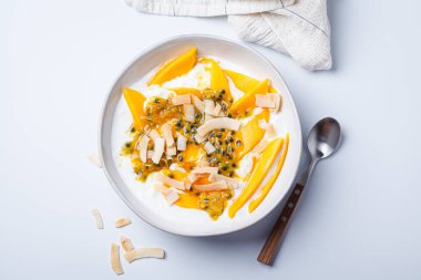 Mangolu kahvaltılık süzme peynir, beyaz arka planda tutku meyvesi ve hindistan cevizi cipsi..