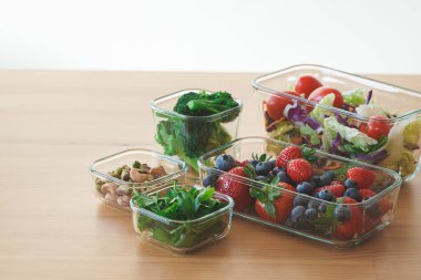 Tahta masadaki cam kaplarda bir hafta için sağlıklı vejetaryen yemekleri. Sebze, fındık, kutuda böğürtlen.