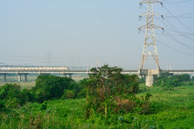 High-voltage power lines and a futuristic train bridge cross a vibrant, natural environment, symbolizing the intersection of technology and the outdoors.