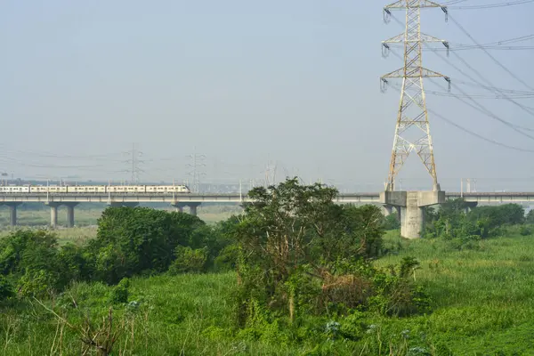 High-voltage power lines and a futuristic train bridge cross a vibrant, natural environment, symbolizing the intersection of technology and the outdoors.