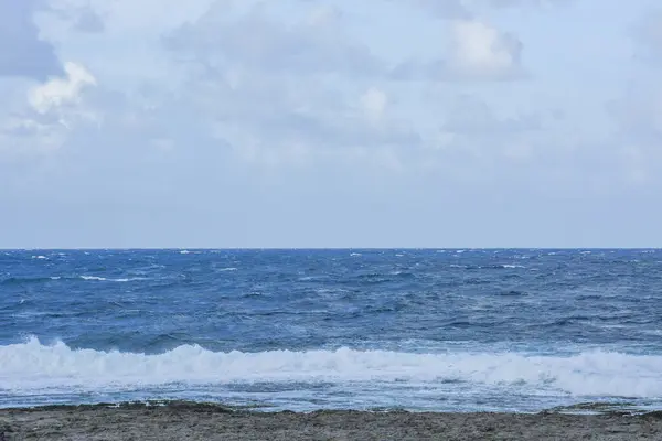 Rough Ocean Waves Impacting a Rocky Beach: A powerful scene of wind-driven ocean waves crashing and creating sea spray as they hit a dark, rocky shore.