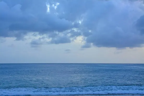 Ocean Waves Under Heavily Cloudy Sky : A wide view of the ocean with waves breaking on the shore under a heavily cloudy, almost overcast sky.