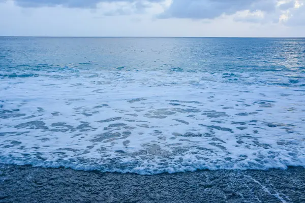 Turbulent Waves Meeting a Dark Pebble Shoreline: A dynamic scene of foamy ocean waves reaching a beach composed of dark pebbles. Coastal Scene: dark pebbles and foaming ocean waves.