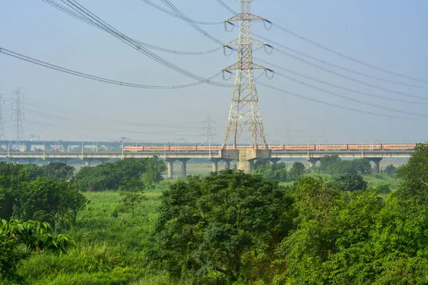 Elevated train track with a high-speed rail, lush greenery, and an electric tower in the countryside.