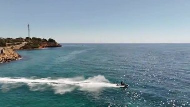Açık denizde su püskürtücü ve açık mavi gökyüzüyle jet ski süren bir adamın hava aracı görüntüleri. Seyahat, tatil, yaz ve macera kavramları için mükemmel..
