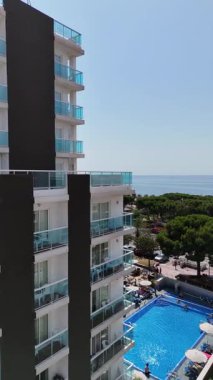 İspanya, Malgrat de Mar 'da balkonları ve yüzme havuzu olan modern bir otelin insansız hava aracı görüntüsü. Güneşli bir günde turistlerin dinlendiği, yeşil ağaçların ve Akdeniz 'in çekildiği manzaralı bir yaz tatili..