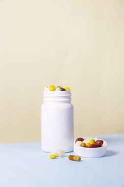 Vitamins and supplements with a white bottle on vanilla and blue color background. Including multi vitamins, vitamin B, C, D, collagen tablets, probiotics capsules and iron capsules.