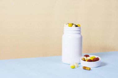 Vitamins and supplements with a white bottle on vanilla and blue color background. Including multi vitamins, vitamin B, C, D, collagen tablets, probiotics capsules and iron capsules.