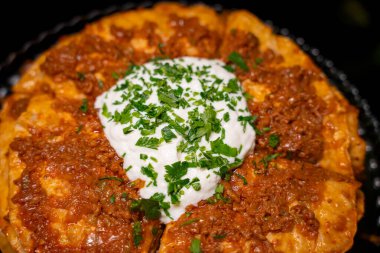 Traditional Turkish food Kayseri Yaglamasi with minced meat, oily, tomato paste and topped with yogurt. Layered yaglama dish with parsley on black background. Anatolian cuisine and flavors concept