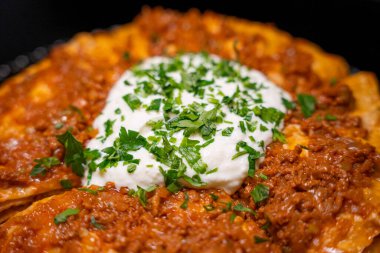 Traditional Turkish food Kayseri Yaglamasi with minced meat, oily, tomato paste and topped with yogurt. Layered yaglama dish with parsley on black background. Anatolian cuisine and flavors concept