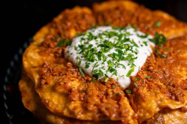 Traditional Turkish food Kayseri Yaglamasi with minced meat, oily, tomato paste and topped with yogurt. Layered yaglama dish with parsley on black background. Anatolian cuisine and flavors concept