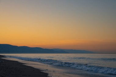 Kumsalda gün batımı ve dağlar. Ufku olan akşam plajı manzarası. Siluet, doğa, sükunet, manzara harikası ve kutsal güzellik konsepti