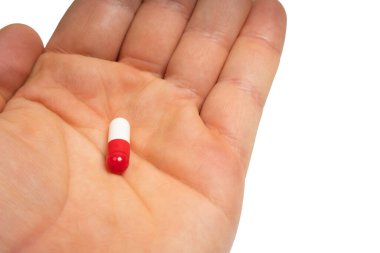 Hand holding red capsule on isolated white background. Red pill in human palm. Medicine, health, treatment and pharmaceutical concept. Close-up
