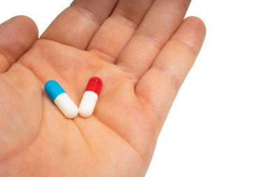 Hand holding blue and red capsules on isolated white background. Two pills in human palm. Choice between. Medicine, health, treatment and pharmaceutical concept. Close-up
