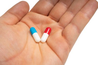 Hand holding blue and red capsules on isolated white background. Two pills in human palm. Choice between. Medicine, health, treatment and pharmaceutical concept. Close-up
