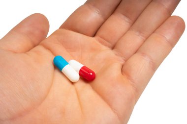 Hand holding blue and red capsules on isolated white background. Two pills in human palm. Choice between. Medicine, health, treatment and pharmaceutical concept. Close-up