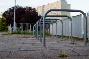 Birçok bisiklet rafı yeşil çimenler ve metal çitlerle çevrili bir kaldırımda boş oturur, öğleden sonra geç saatlerde arka planda uzun bir konut binası durur..