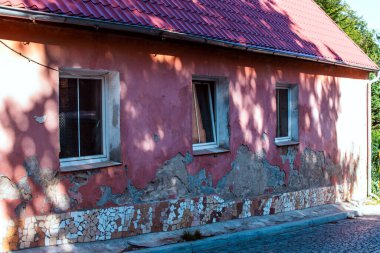 Eski pembe bir evde yıpranmış boya ve çatlak duvarlar var. Güneş ışığı gölgeler oluşturur, sakin bir mahallede yıpranmış dokusunu vurgular..