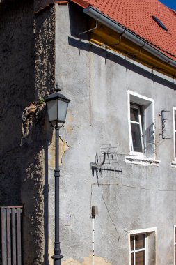 Eski bir bina, gri boyası ve kırmızı çatısı olan klasik bir sokak lambasının yanında. Açık mavi gökyüzünün altında sessiz bir mahallenin cazibesini yakalıyor..