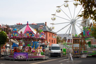 Parlak karnaval gezileri ve şehir meydanını dolduran dev bir dönme dolap. Açık bir gökyüzü altında neşeli bir güne hazırlanırken renkli dekorasyonlar ziyaretçileri cezbediyor..