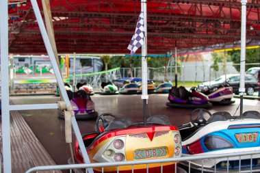 Çarpışan arabalar bir karnavalda kırmızı bir gölgeliğin altında boş boş otururlar. Sahne canlı, parlak renkler ve yaklaşan şenlik etkinlikleri için beklenti dolu..