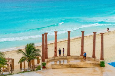 Cancun, Meksika - 3 Ocak 2022: İnsanlar yağmurdan sonra eski tarz sütunlar ve turkuaz okyanus manzaralı huzurlu bir Cancun plajının keyfini çıkarıyorlar. Yüksek kaliteli fotoğraf.