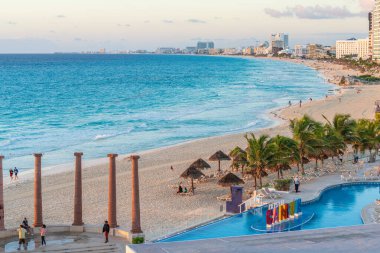 Cancun, Meksika - 6 Ocak 2022: Turkuaz suları, tatil köyleri, palmiye ağaçları ve günbatımında parlak bir ufuk çizgisi olan Cancuns sahilinin panoramik manzarası.