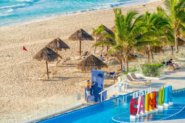 Cancun, Meksika - 6 Ocak 2022: Cancun 'daki tropik tatil beldesi sahnesi şezlonglu sandalyeler, sazdan şemsiyeler, palmiye ağaçları ve renkli havuz kenarı Cancun tabelası yüksek kaliteli fotoğraf.