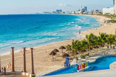 Cancun, Meksika - 6 Ocak 2022: Turkuaz sular, kumlu plaj, tatil havuzu ve açık mavi gökyüzü altında renkli Cancun tabelası bulunan Cancun sahili manzarası.
