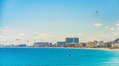 Cancun Otel Bölgesi 'nin güneşli bir günde deniz paraşütçüleri, botlar ve turkuaz suların ve sahil kenarındaki tatil yerlerinin keyfini çıkaran kalabalıklarıyla dolu renkli bir sahnesi..