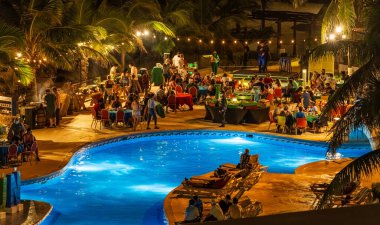 Cancun, Meksika - 7 Ocak 2022 Cancun Hotel Zone 'da insanların yemek yediği, sosyalleştiği ve sicim ışıkları ve palmiye ağaçları altında tropikal titreşimlerin tadını çıkardığı canlı bir akşam havuz başı partisi.