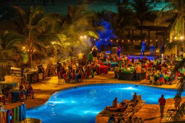 Cancun, Meksika - 7 Ocak 2022 Cancun Hotel Zone 'da gece havuzu kutlamaları canlı müzik, renkli ışıklandırma ve konukların palmiye ağaçları altında yemek ve içeceklerden keyif almaları..