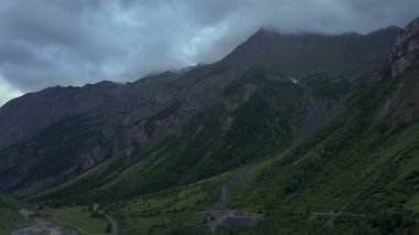 Beyaz ve gri bulutlarla dolu bir gökyüzünün altındaki vadinin her iki tarafında uzun dağlar. Dramatik ve atmosferik sahne, doğa, manzara, seyahat ve sinema projeleri için mükemmeldir..