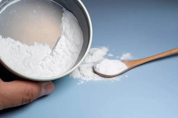 Ucunda az miktarda beyaz toz olan bir parmak, aynı tozdan bir kabın üzerinde asılı duruyor..