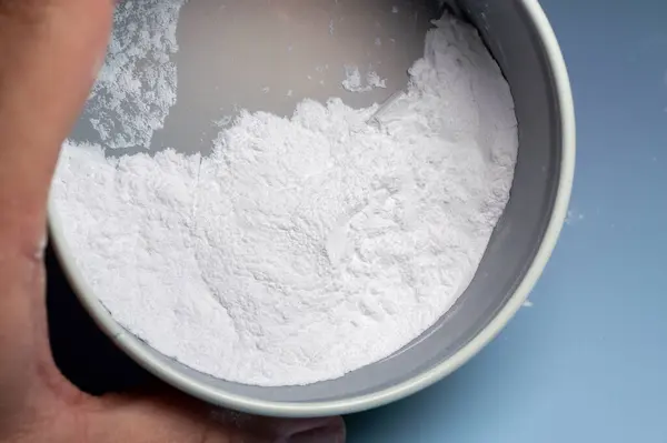 Ucunda az miktarda beyaz toz olan bir parmak, aynı tozdan bir kabın üzerinde asılı duruyor..