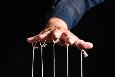 İnsan 'ın Yakın Çekimi Kuklayı Parmaklarıyla Kontrol Ediyor. Man 's Hand, parmakları siyah arkaplan ve manipülasyon konseptine bağlı olan kuklayı kontrol eder.