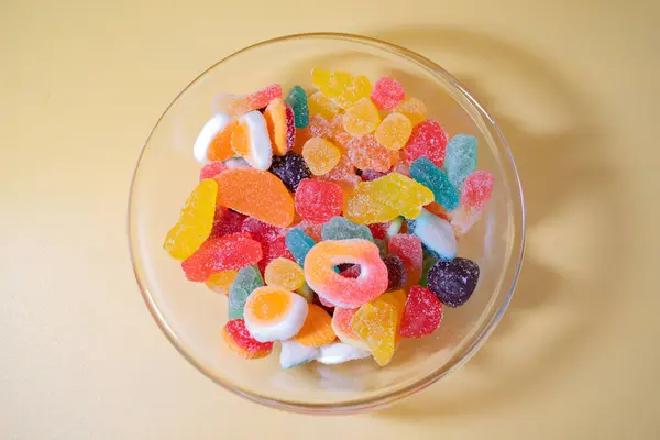 Sarı arka planda çeşitli canlı, şeker kaplı şekerlerle dolu cam bir kasenin genel manzarası..